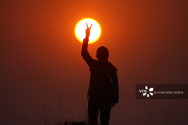 日落时分，一个孩子做胜利手势的剪影图片素材