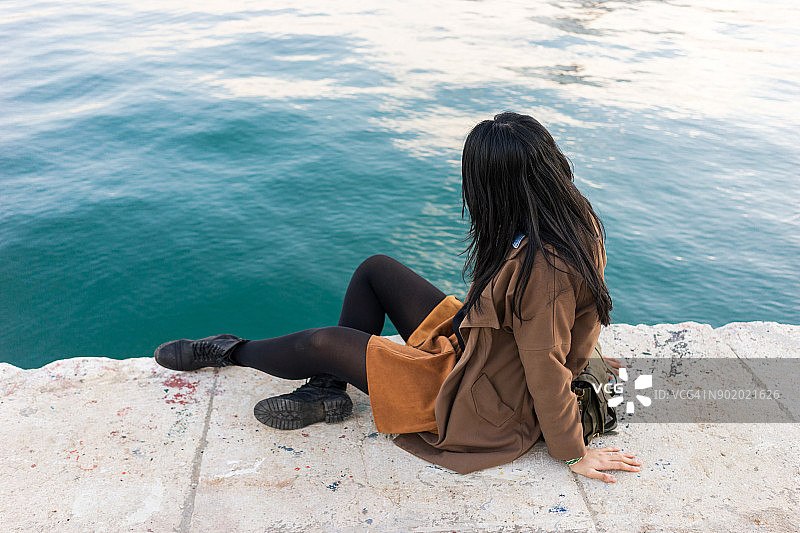 在西班牙安达卢西亚的马拉加，一名年轻女子在Palmeral de las sorpresas港口的海岸线上休息。图片素材