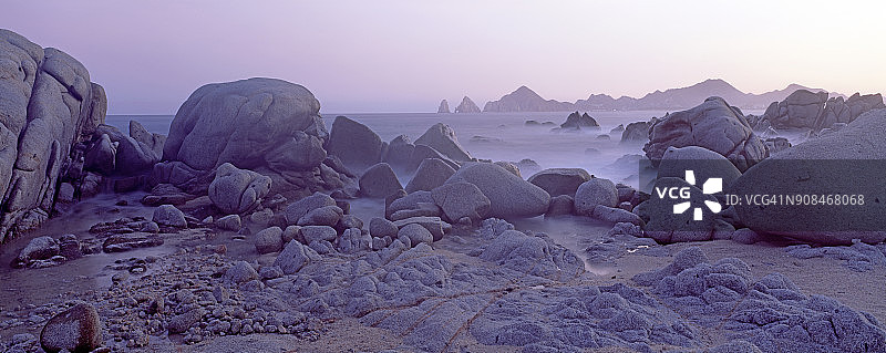 黄昏时，沿着海岸线的巨石和岩石的全景图，背景是卡波圣卢卡斯拱门。图片素材