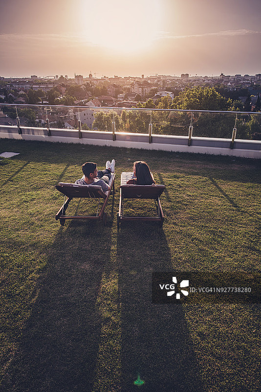 上面的观点，微笑的夫妇在顶层露台的躺椅上交谈。图片素材