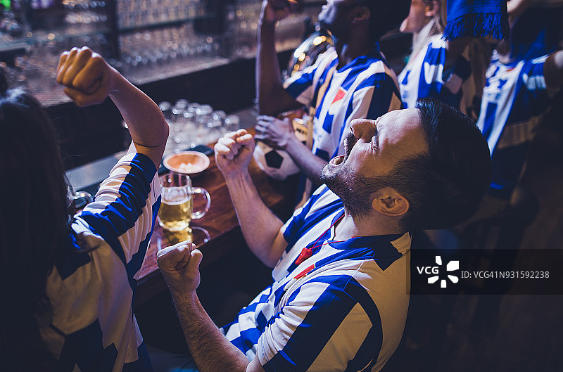 球迷们一边在酒吧里看电视比赛，一边庆祝他们的足球队的胜利。图片素材