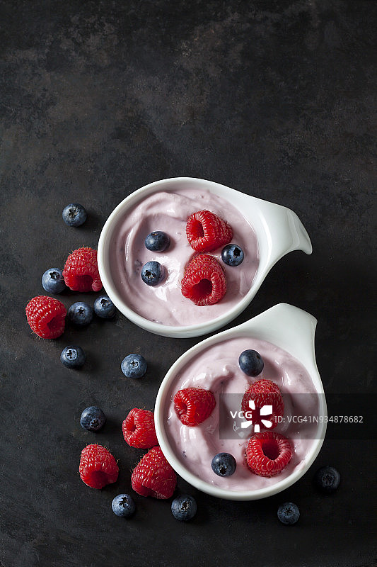 两碗水果酸奶，蓝莓和覆盆子放在深色的地面上图片素材