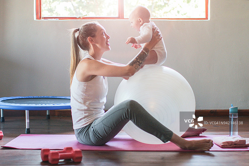 一位年轻的母亲和她的男婴在家里锻炼身体。图片素材