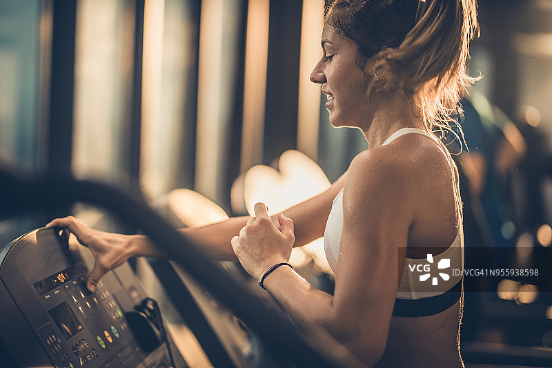 在健身房跑步机上慢跑时，女运动员调整速度的侧面视图。图片素材