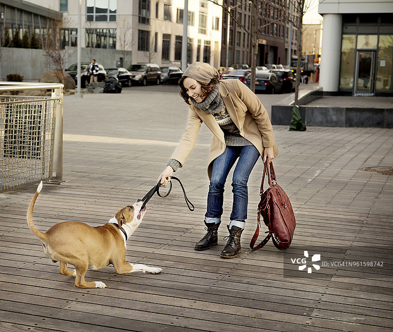 在城市的人行道上，一名妇女牵着狗狗的皮带图片素材