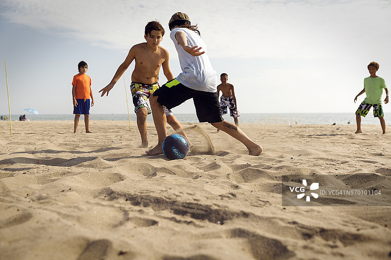 朋友们在沙滩上对着大海踢足球图片素材