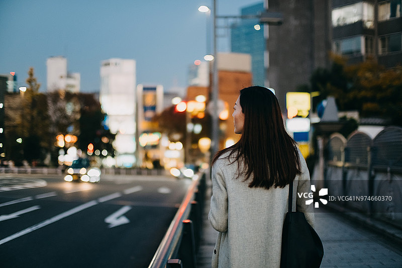 黄昏时分，一个年轻女子在市中心的街道上等待出租车图片素材