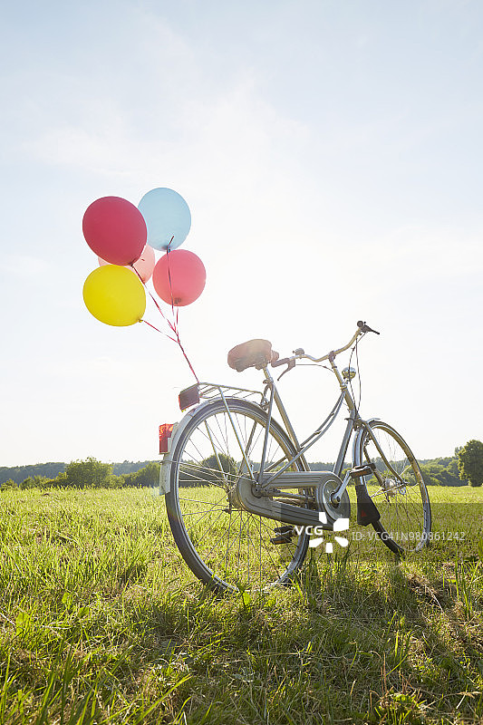骑着彩色气球的自行车在草地上对着天空图片素材