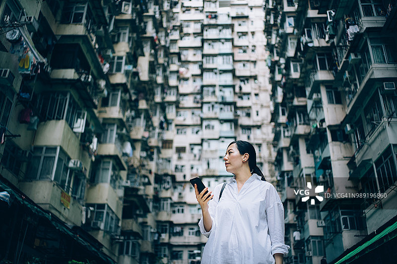 在城市里，年轻女子用手机对抗古老传统的住宅建筑图片素材