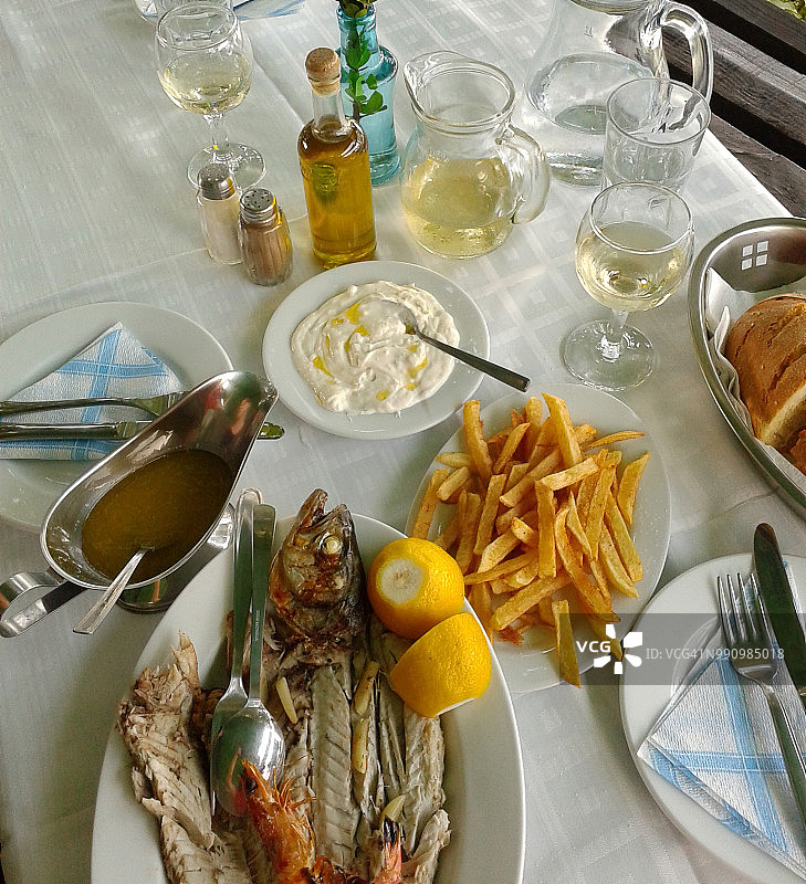 在一个典型的希腊酒馆用餐。供应鱼、炸薯条和Tsatsiki。移动设备拍摄图片素材