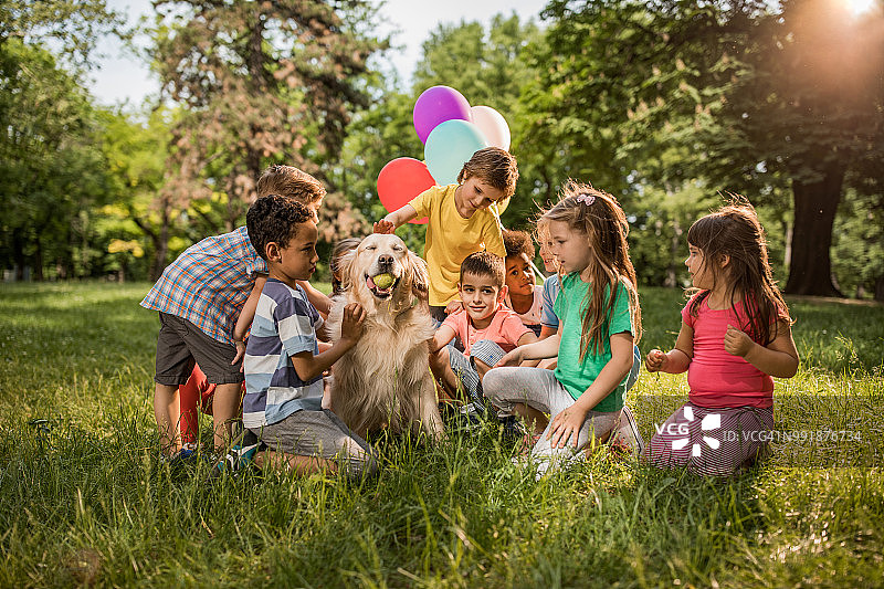 春天的一天，可爱的孩子们和金毛猎犬在公园里嬉戏。图片素材