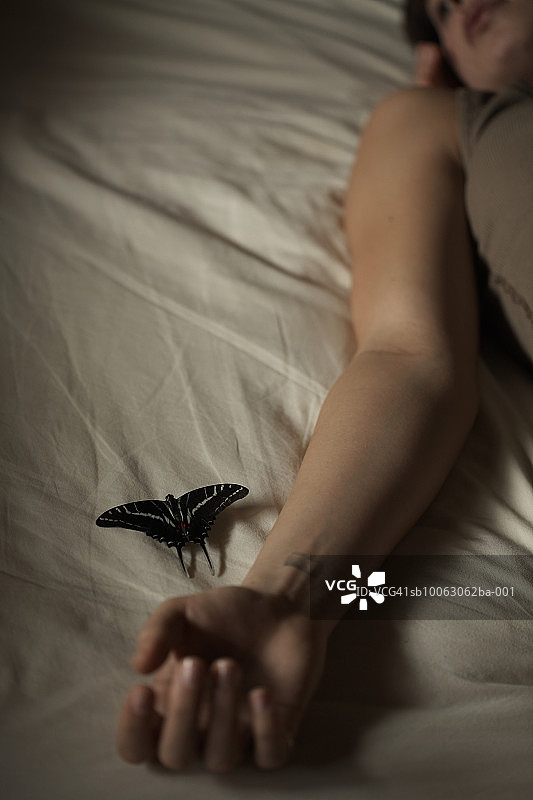 女人躺在床上，蝴蝶靠近她的手图片素材