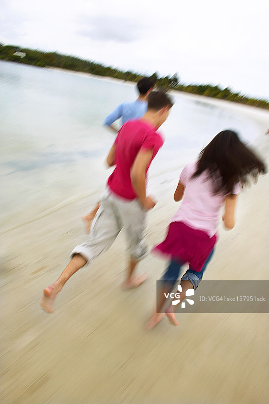 三个青少年朋友(16-18岁)在海滩上跑步的特写图片素材