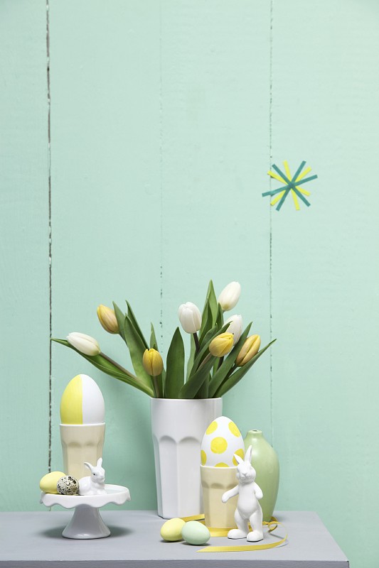 柔和的复活节安排;郁金香在陶瓷烧杯，鸡蛋和兔子饰品图片素材