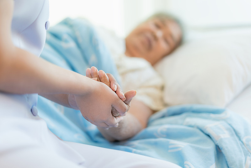 护士坐在病床上，旁边是一位老妇人在帮忙图片素材