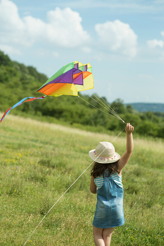 抱着风筝的女孩背对天空在田野上行走的背影图片素材