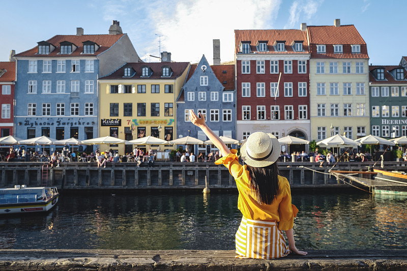 年轻女子坐在色彩斑斓的建筑前，沿着尼哈芬，丹麦哥本哈根图片素材