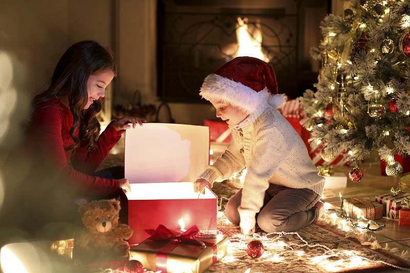 圣诞节期间，孩子们在树旁打开礼物。图片素材