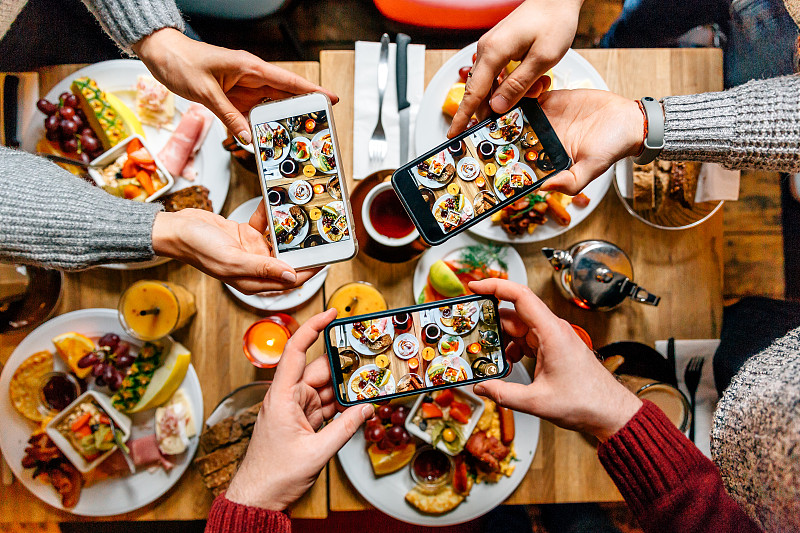 朋友们在餐厅吃早午餐时用智能手机拍桌上的食物图片素材