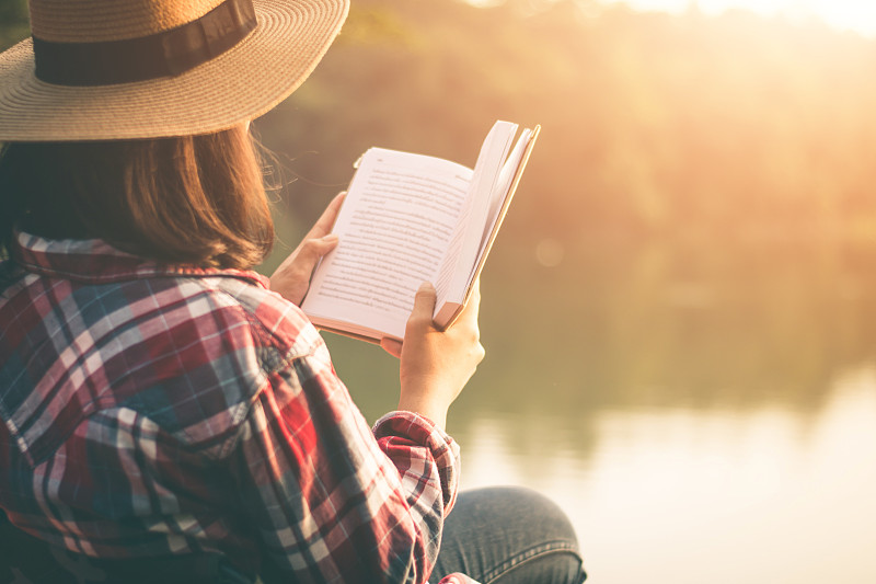日落时分坐在湖边看书的女人的侧视图图片素材