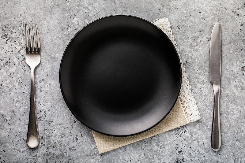 空陶瓷盘在黑色与刀叉的桌子上，俯视图图片下载