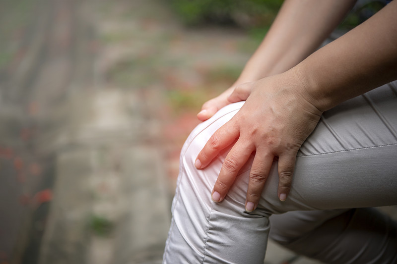 一位老妇人在公园里饱受膝盖疼痛之苦。抱着膝盖，用手按摩。图片下载