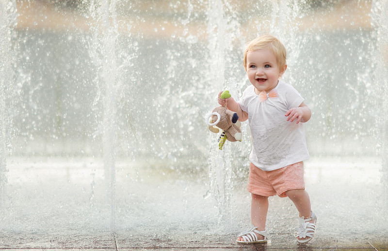 可爱的蹒跚学步的小女孩走过喷泉在夏天，笑着图片下载