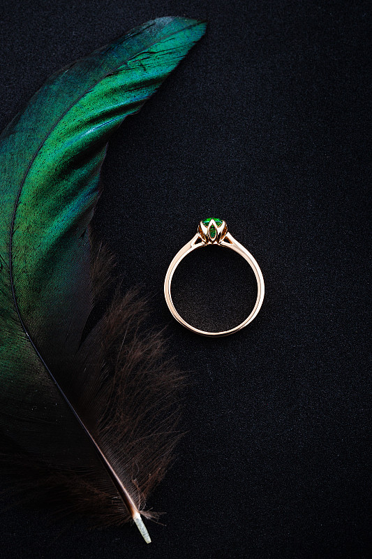 结婚戒指与祖母绿宝石在黑色背景和绿色羽毛图片素材