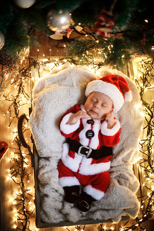 新生儿在圣诞老人的衣服躺在圣诞树下。图片素材