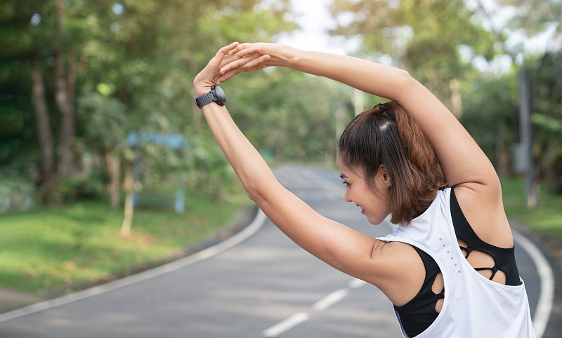 女人在跑步或锻炼前做伸展运动。年轻女性跑步者在早晨跑步前伸展手臂。健身和健康生活理念。图片素材