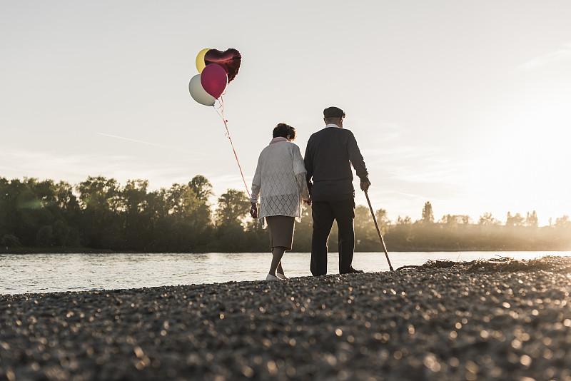 老夫妇与气球漫步在傍晚的河边背影图片素材