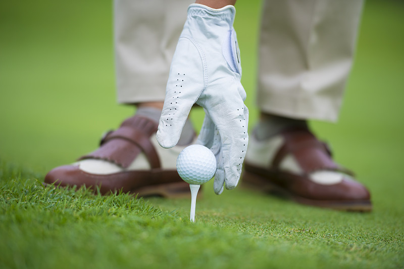 优雅的高尔夫球手戴着手套把高尔夫球放在球座上图片下载