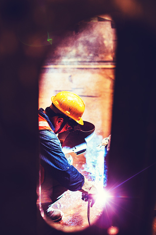 小景是一个蓝领工人在工厂忙着焊接一些金属零件。图片素材