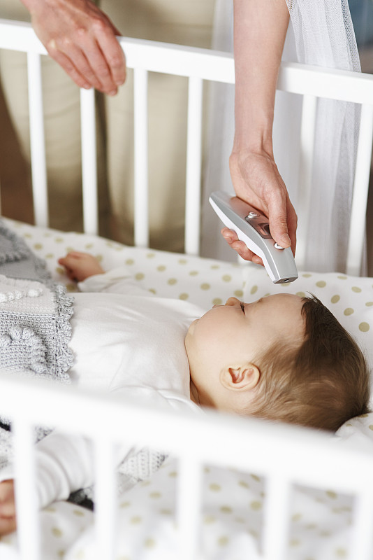 母亲用数字温度计检查婴儿在婴儿床的温度图片下载
