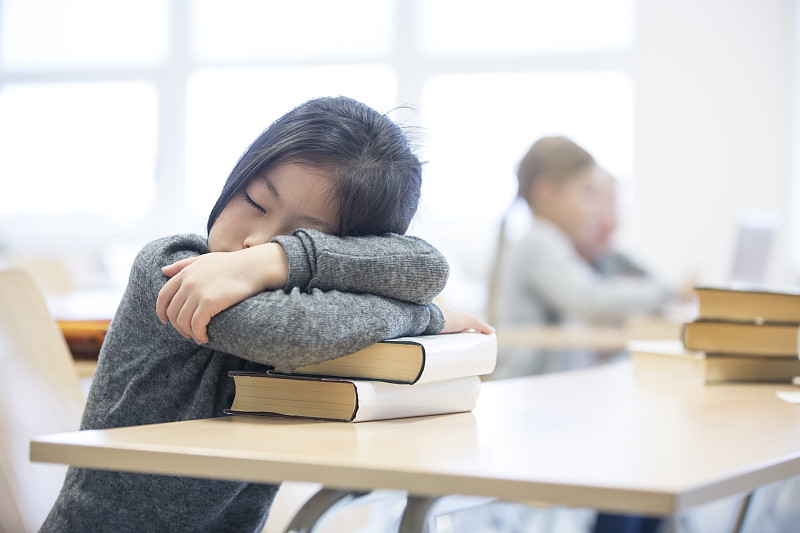 一个女学生在学校桌子上的一堆书上睡觉图片下载