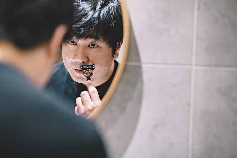 一个亚裔华人在洗手间对着镜子刮胡子图片下载