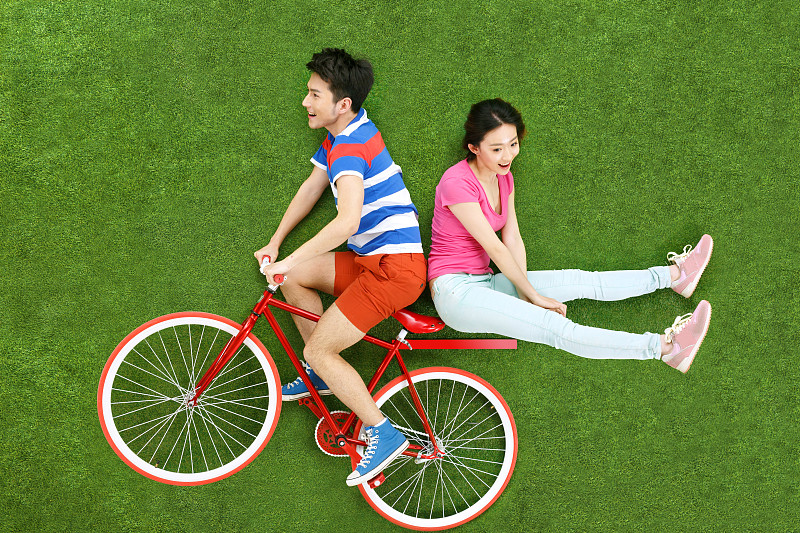 青年情侣在草地上骑自行车图片下载