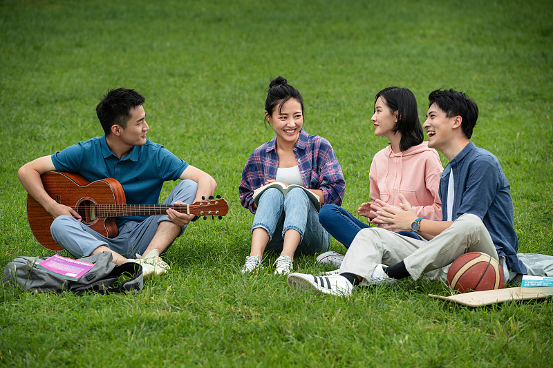 快乐的大学生在草地上弹吉他唱歌图片素材