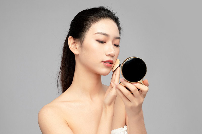 灰色背景里正在使用粉饼的亚洲美女面部特写，化妆护肤整容图片下载