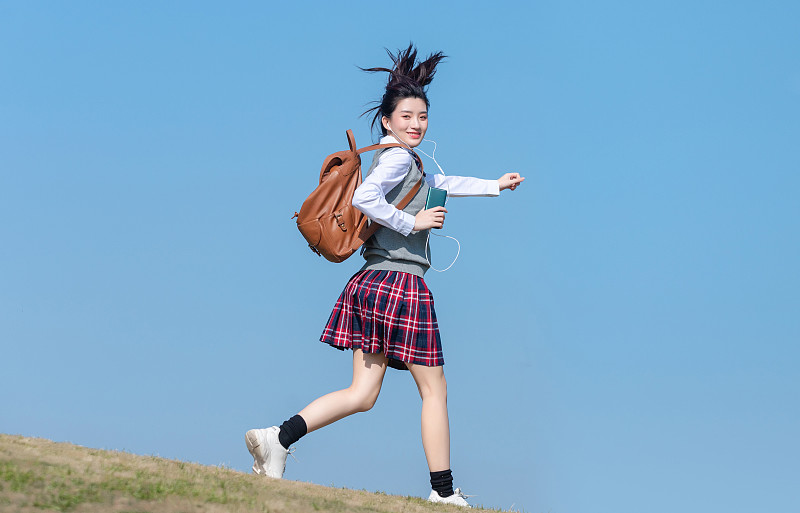 蓝色天空背景下，正在慢跑的亚洲女学生图片下载