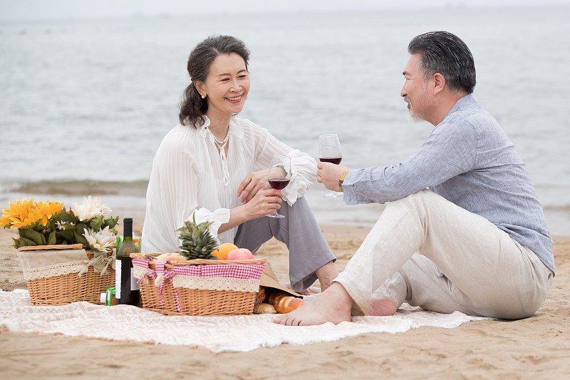 幸福的老年夫妇坐在海滩上野餐饮酒图片素材