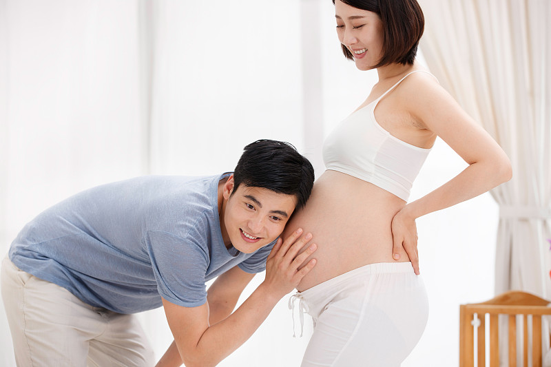 年轻父亲抚摸孕妇的肚子聆听胎儿图片下载