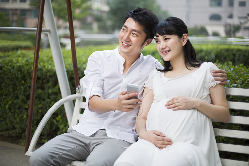 丈夫和怀孕的妻子在摇椅上听音乐图片素材