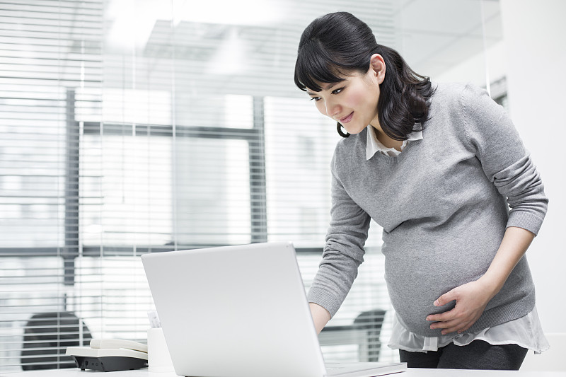 怀孕的商务女士在办公室使用笔记本电脑图片素材