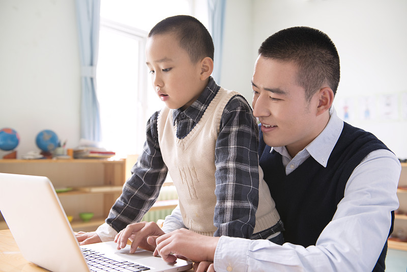 Kindergarten teacher and boy using laptop图片下载