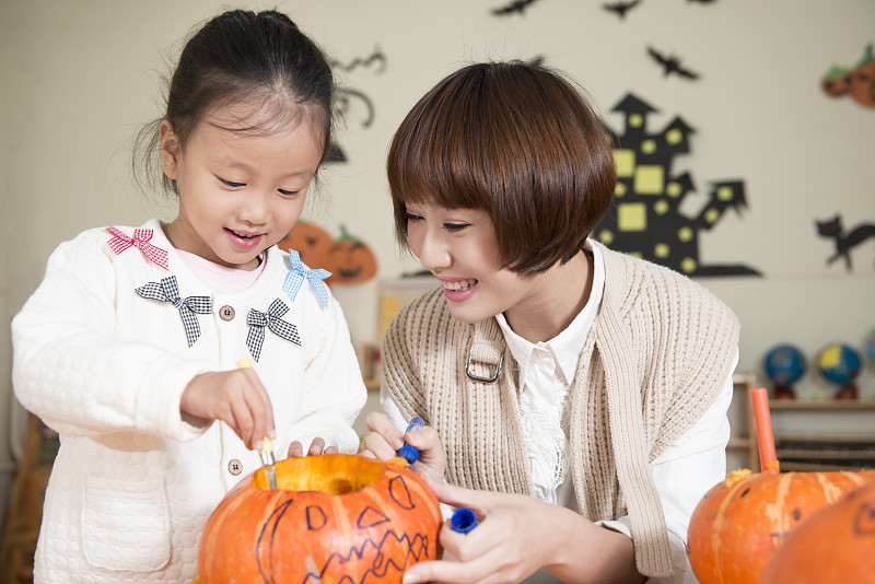 Kindergarten teacher and girl carving pumpkin图片下载