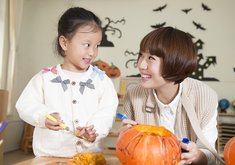 Kindergarten teacher and girl carving pumpkin图片下载