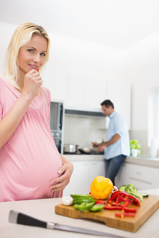 怀孕微笑的女人和切碎的蔬菜和男人在厨房做饭的房子图片下载