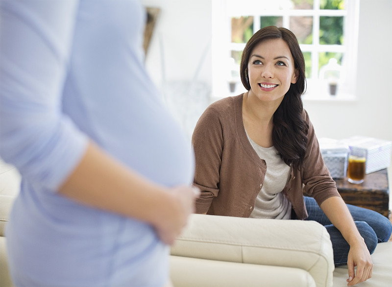 女人对着怀孕的朋友微笑图片素材