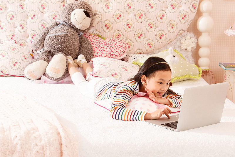 小女孩在床上使用笔记本电脑图片素材